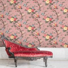 a red chair sitting in front of a pink wallpapered with flowers and vines