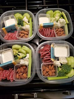 four plastic containers filled with assorted food items on top of an oven burner