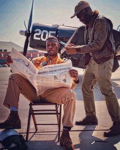 two men sitting in chairs looking at a paper with an airplane on the ground behind them