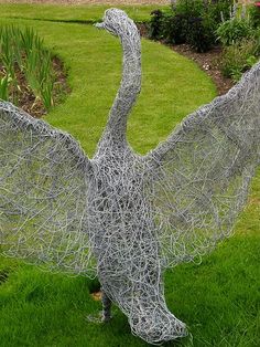 a large metal bird sculpture sitting on top of a lush green field