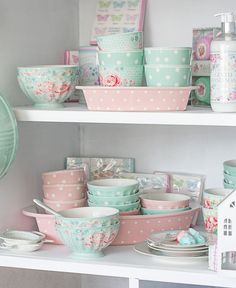 the shelves are filled with bowls and dishes in pastel pinks, mint green and white