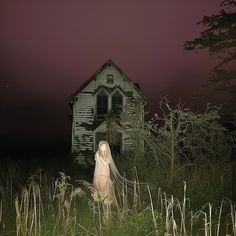 a ghostly woman standing in front of an old house at night with the light on