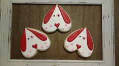 three decorated cookies in the shape of dogs with hearts on them are hanging from a white frame