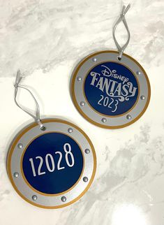 two metal tags with disney fantasy 2013 on them sitting on a marble countertop next to each other