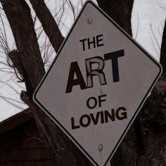 a sign that says the art of loving hanging on a tree in front of a house