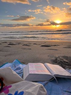 an open book sitting on top of a blanket next to the ocean