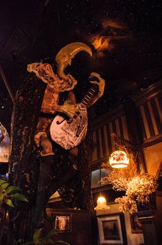 a guitar is hanging from a tree in a room filled with plants and lights at night