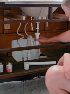 a man fixing a sink in a bathroom under a counter top with other items on it