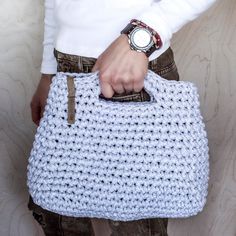 a person holding a crocheted purse in their hand with a watch on it