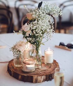 flowers and candles are arranged in mason jars on a wood slice at a wedding reception