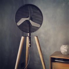 a black fan sitting on top of a wooden tripod next to a white vase