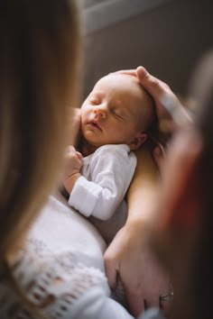 a woman holding a baby in her arms while it is being held by another person