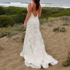 a woman in a wedding dress standing on the beach looking at the ocean with her back to the camera