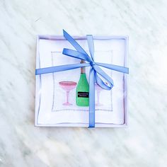 a glass and bottle wrapped in blue ribbon on a white marble table with a gift box