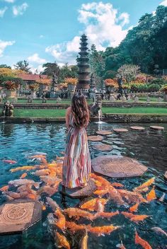 a woman standing on the edge of a pond surrounded by fish