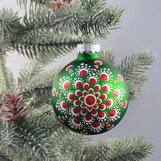 a green christmas ornament hanging from a pine tree with red and white designs on it