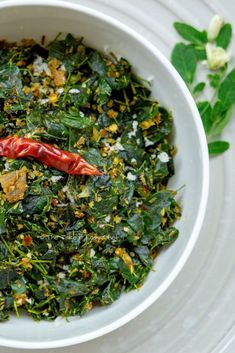 a white bowl filled with food on top of a table next to green leaves and flowers