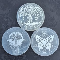 three glass plates with designs on them sitting on a black tableclothed surface, one has a butterfly and the other is a tree