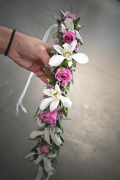 a hand holding a flower lei with pink roses and white orchids on the side