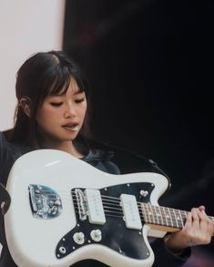 a woman holding a white guitar in her right hand and looking down at the ground