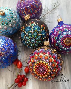 several ornaments are sitting on the floor with red berries around them and one is painted in bright colors