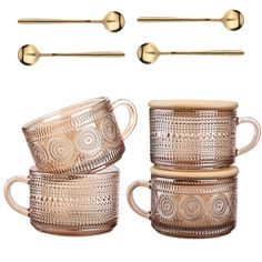 four golden coffee mugs and two spoons with gold handles on a white background