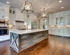 a large kitchen with wooden floors and white cabinets in the center is lit by two chandeliers