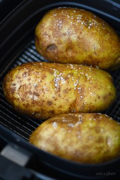 three potatoes sitting in an air fryer on top of a grilling pan with brown stuff all over them