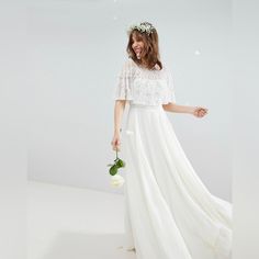 a woman in a long white dress holding a flower and wearing a wreath on her head