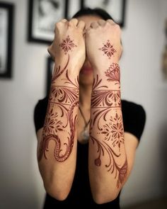 a woman holding her hands to her face with hendi tattoos on both arm and shoulder