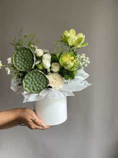 a person holding a white vase with flowers in it and ribbons around the bottom half