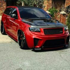 a red and black car parked in front of a brick building next to a sidewalk