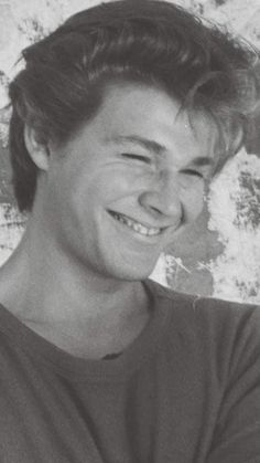 a black and white photo of a young man smiling with his hair in the air