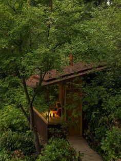 a woman sitting on the porch of a cabin surrounded by trees and greenery at night