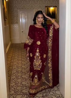 a woman standing in a hallway wearing a maroon and gold dress with an intricate design on it