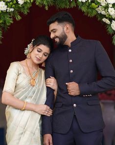 a man and woman standing next to each other in front of a floral arch with greenery