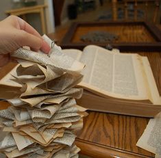 a stack of books sitting on top of a wooden table next to a person's hand