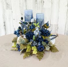 a bouquet of blue flowers and greenery on a table with two votive candles