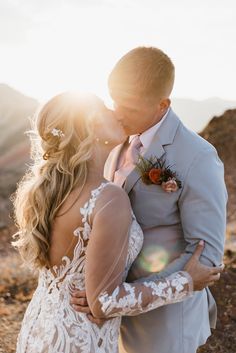 a bride and groom kissing on top of a mountain in the sun light at their wedding