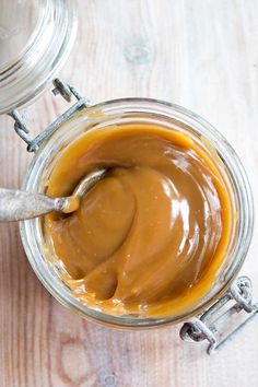 a jar filled with caramel sauce on top of a wooden table next to a spoon