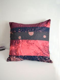 a red and black pillow sitting on top of a white bed next to a wall