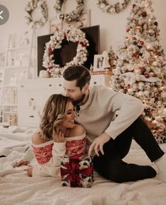 a man and woman sitting on a bed in front of a christmas tree