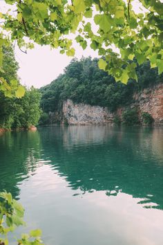 the water is green and clear with some trees around it, as well as cliffs