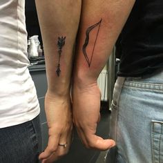 two people holding hands with tattoos on their arms and one has an arrow in the middle