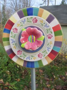 a colorful plate with a flower on it in front of some grass and flowers near a house