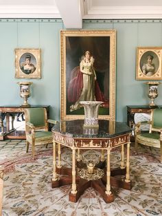 a room with blue walls and paintings on the wall, including an ornate table surrounded by chairs