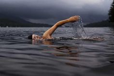 a person swimming in the water with their hand out to catch some air while it's raining