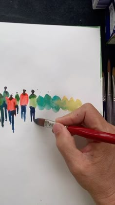 a person is holding a pencil and drawing on paper with watercolors in front of them