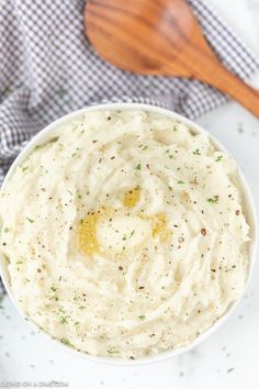 a white bowl filled with mashed potatoes on top of a table next to a wooden spoon