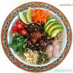 a colorful bowl filled with rice, meat and veggies next to sliced avocado